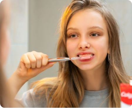 Girl brushing her teeth in front of a mirror as part of a healthy oral health routine.