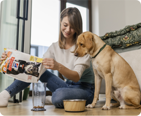 Woman pouring Hill's Pet Nutrition food into a measuring container while a dog looks attentively.
