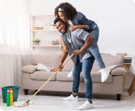 A man gives a piggyback ride to a smiling woman while he holds a mop in a clean room.