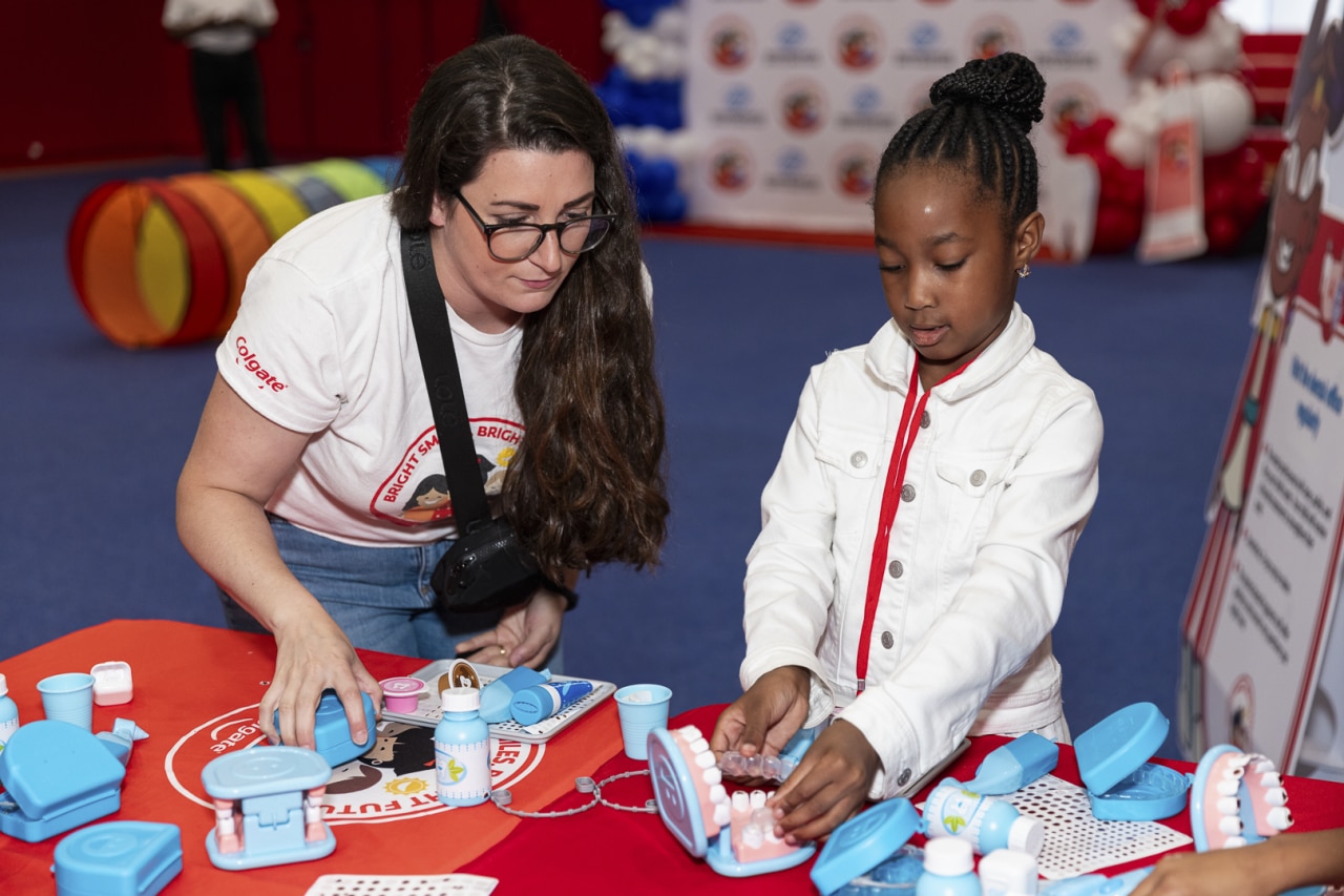 Child places retainer on dental model while standing next to a Colgate educator at a Bright Smiles Bright Future educational event.