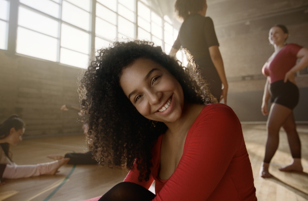 Smiling woman in red workout top at fitness studio during active wellness routine.