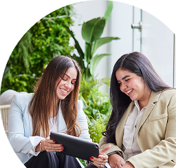 Two women reviewing documents on a tablet in a green and healthy garden.