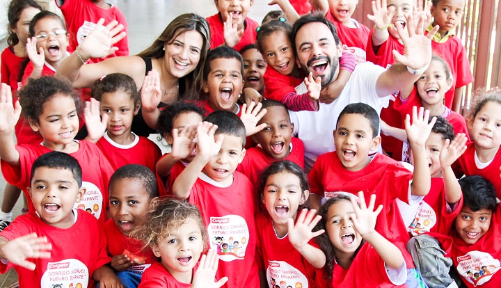 Group of children and adults smiling and waving at the camera while wearing "Bright Smiles, Bright Futures" shirts.