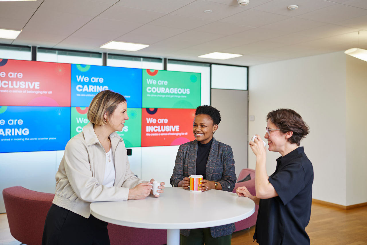 Group of diverse people having a conversation while drinking coffee in front of a wall with multiple Colgate-Palmolive company values.