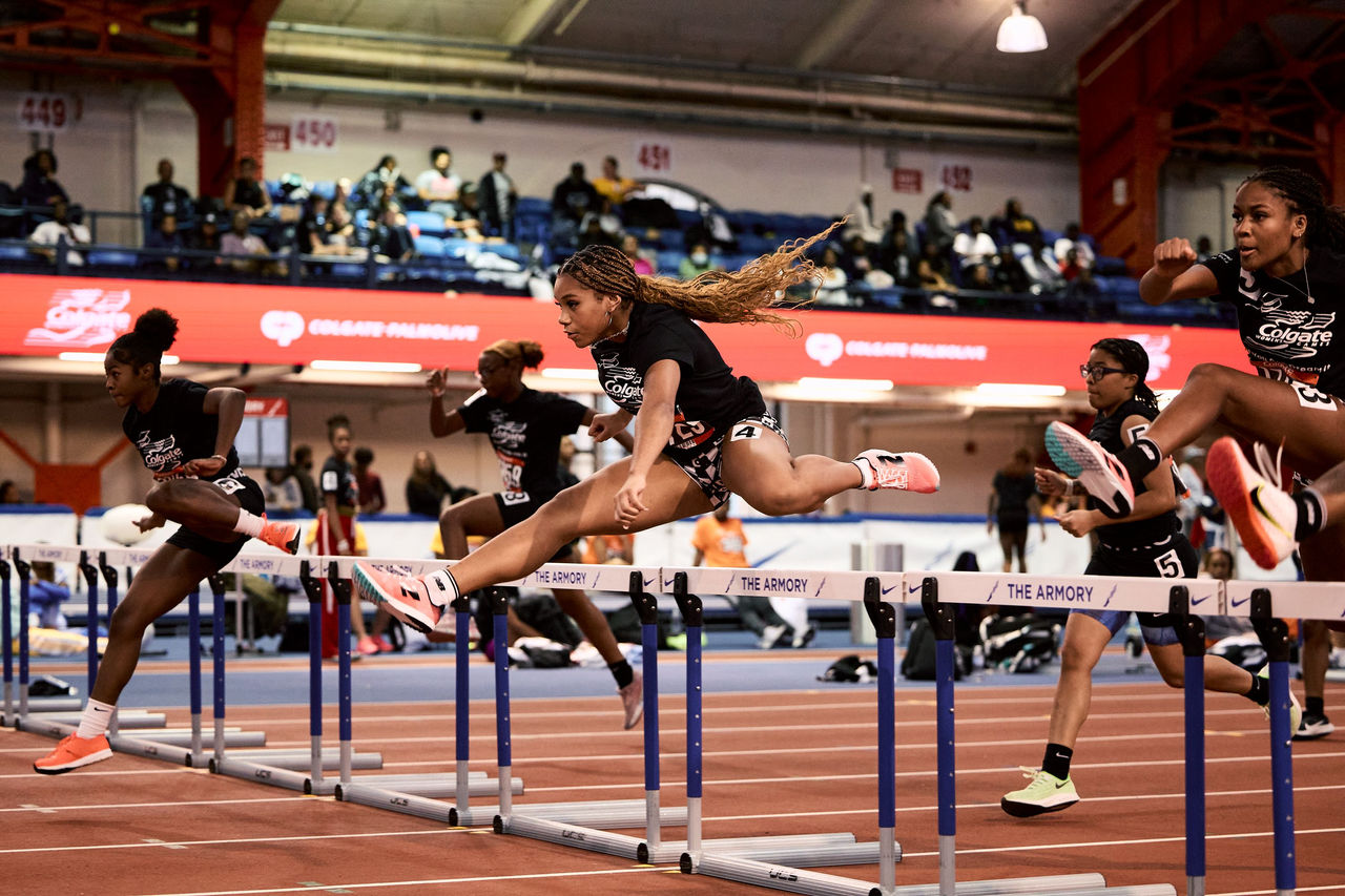 Group of athletes jumping over hurdles on a race track as part of the "Colgate Women's Games".