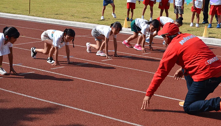 Group of children on a track about to race together as part of an "Estrella Colgate" event.
