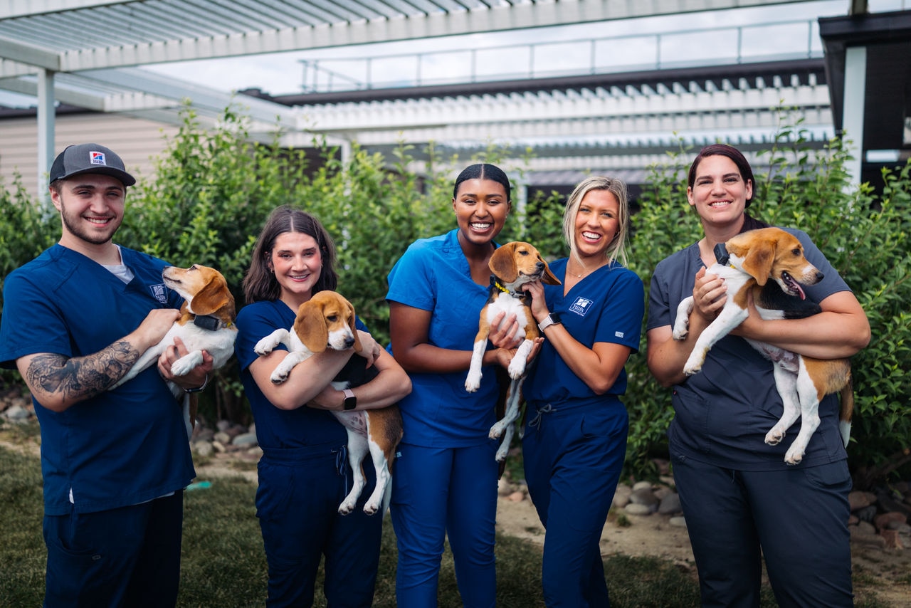 Smiling veterinarians holding dogs, while smiling in front of a pet clinic.