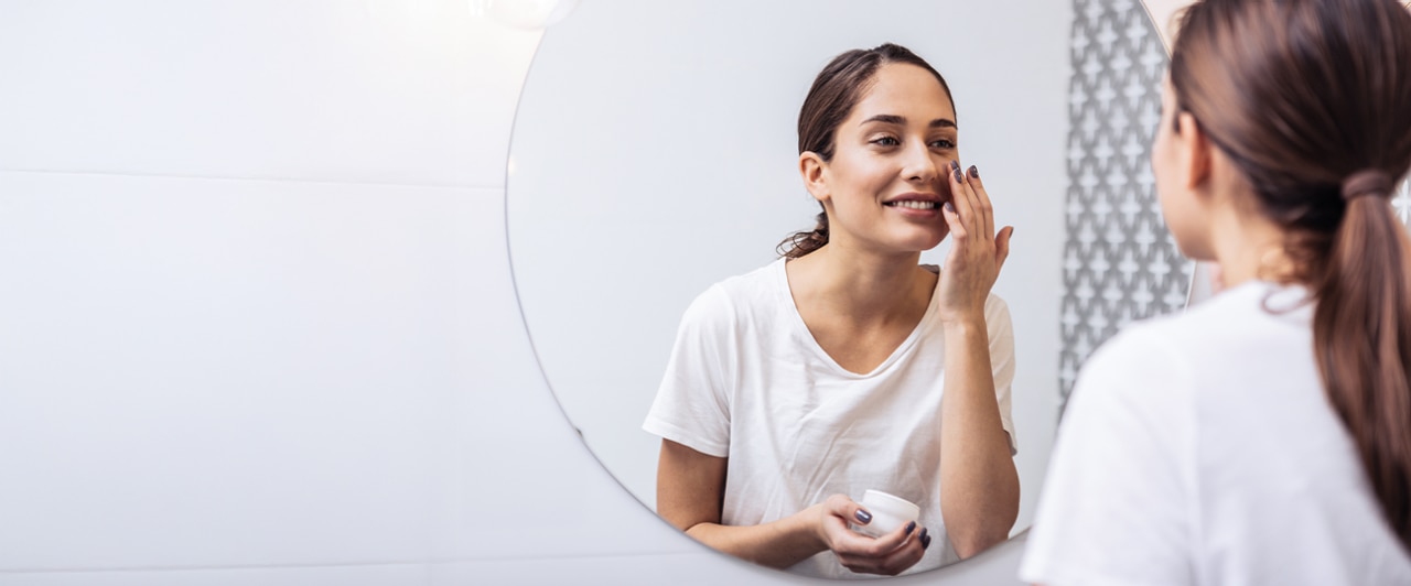 Woman applying skincare products from Colgate-Palmolive for her skin health.