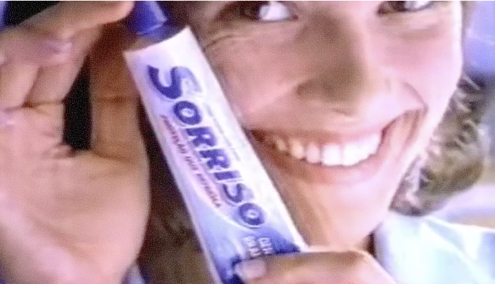 Woman smiling and holding a Sorriso toothpaste tube close to her face in an ad from the 1990s.