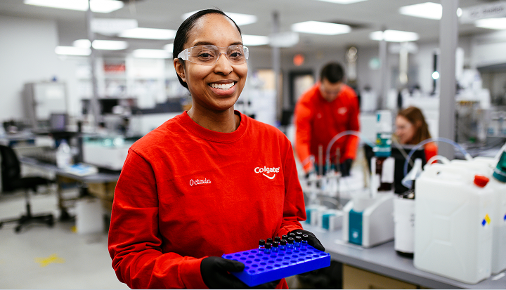 Colgate scientist in red shirt and safety glasses working with laboratory equipment.